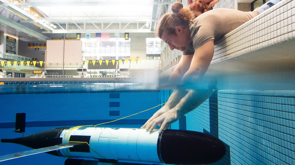 Student holding research glider under the water in a pool.